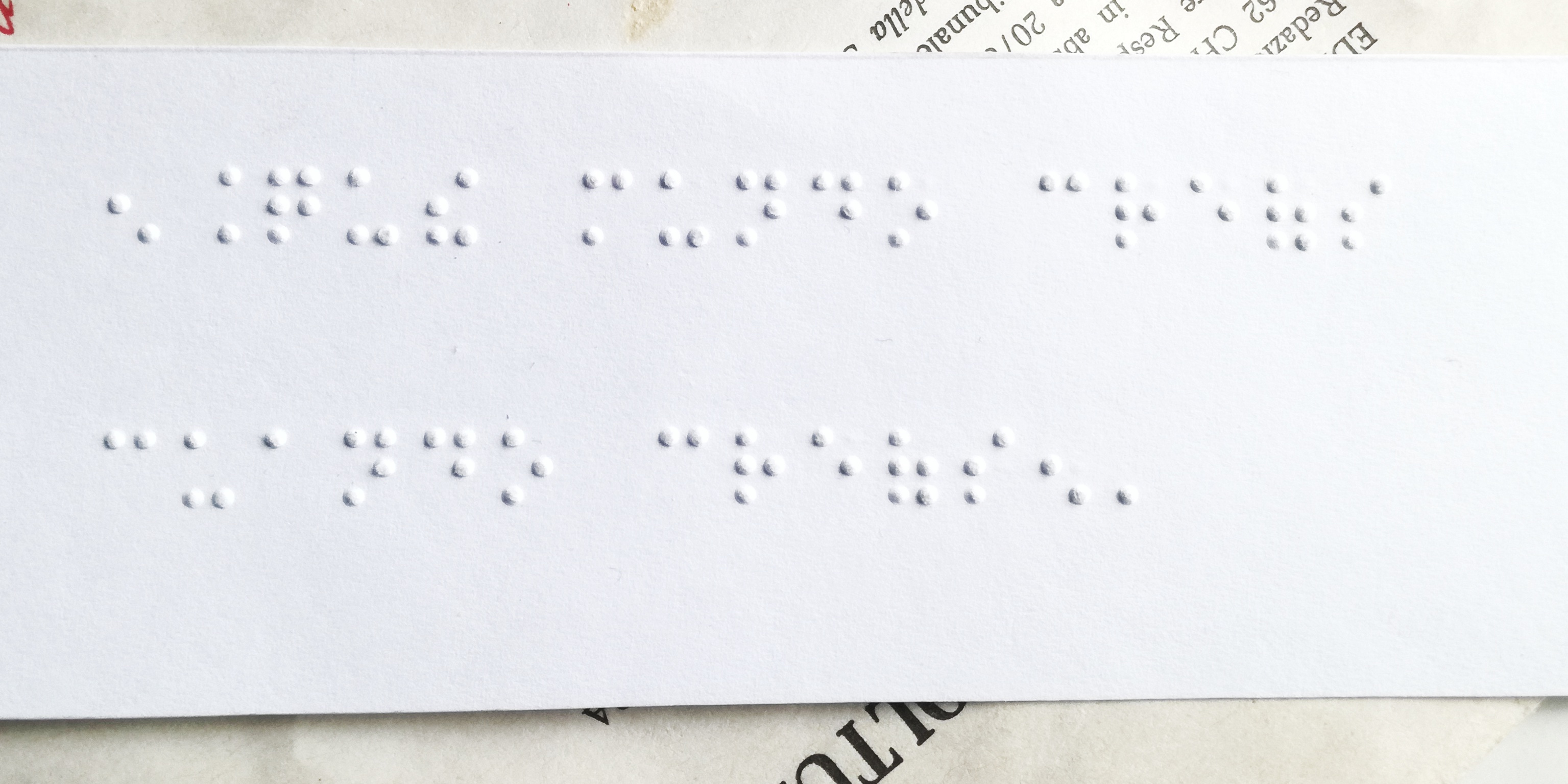 Una hoja impresa en Braille con textura notable, sobre otras que apenas sobresalen alrededor) con textos impreso normalmente. 